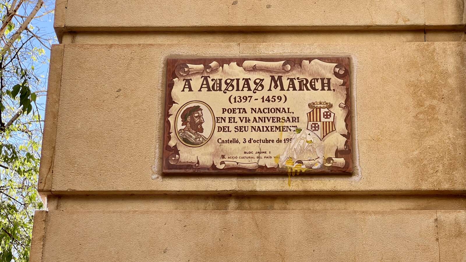 Placa en una paret d’un carrer. El text diu: “A Ausiàs March (1397-1459), poeta nacional, en el sisè aniversari del seu naixement a Castelló, 3 d’octubre de 19… (els últims dígits de l’any no es llegeixen, però s’entén que és 1997).”
